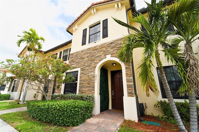 view of exterior entry featuring stucco siding, stone siding, and a tile roof