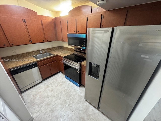 kitchen featuring dark countertops, stainless steel appliances, brown cabinetry, and a sink