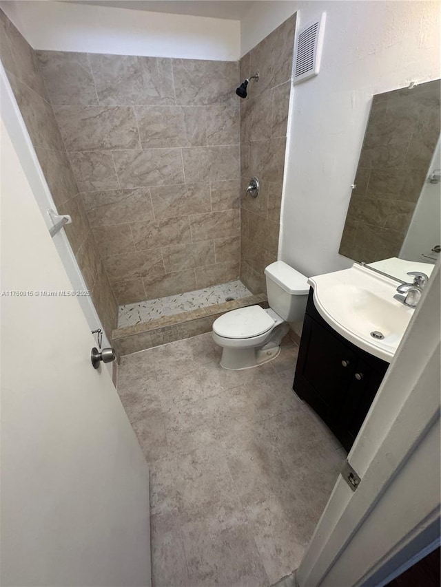 full bathroom with visible vents, toilet, tiled shower, and vanity