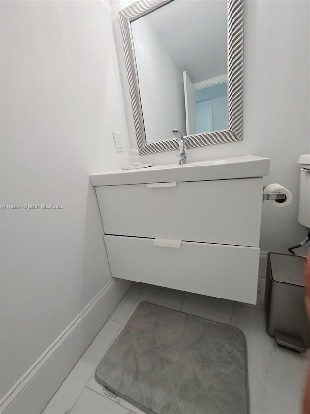 half bath with baseboards, toilet, and vanity