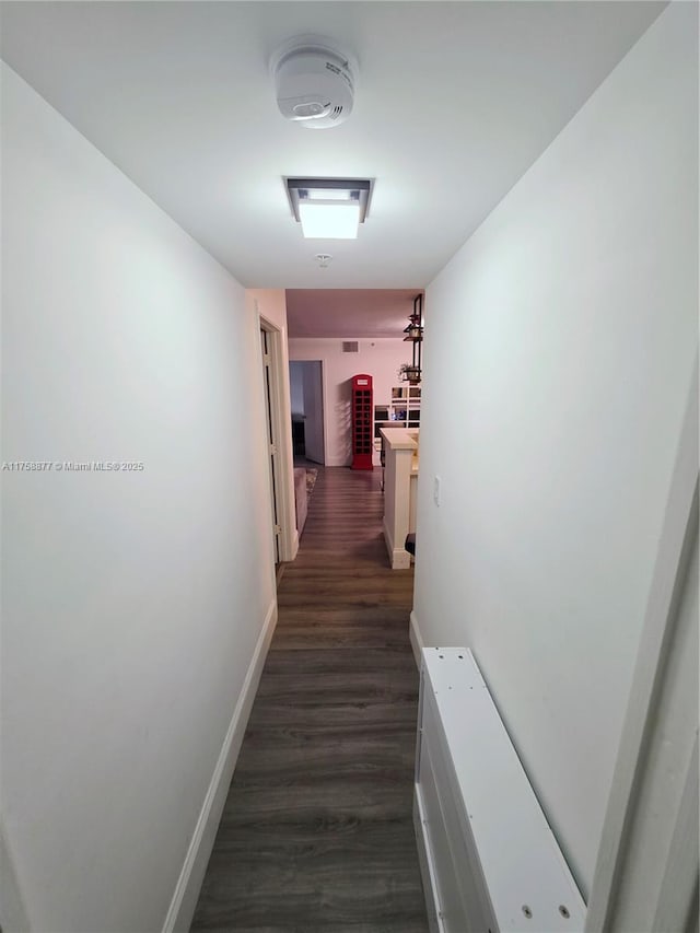 corridor featuring dark wood-type flooring and baseboards