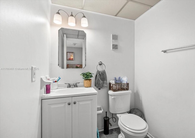 half bathroom featuring visible vents, baseboards, toilet, vanity, and a paneled ceiling