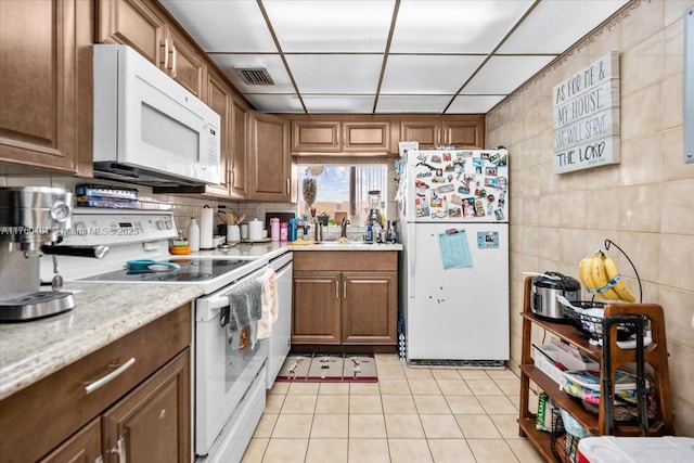 kitchen featuring backsplash, light tile patterned flooring, white appliances, tile walls, and a sink