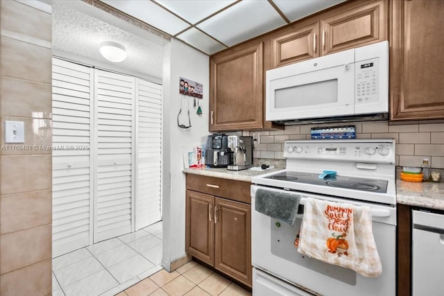 kitchen featuring decorative backsplash, white appliances, light tile patterned floors, and light countertops