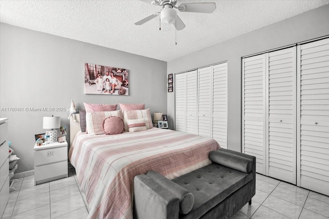 bedroom featuring light tile patterned flooring, a ceiling fan, multiple closets, and a textured ceiling