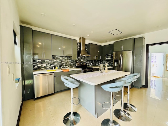 kitchen with wall chimney range hood, light countertops, stainless steel appliances, light tile patterned floors, and a kitchen bar