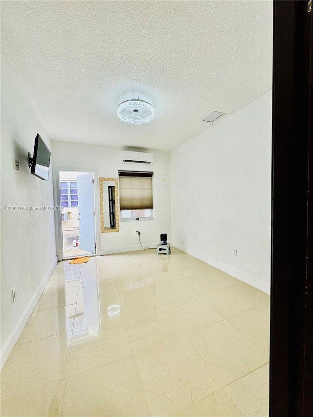 spare room with a textured ceiling, an AC wall unit, and baseboards