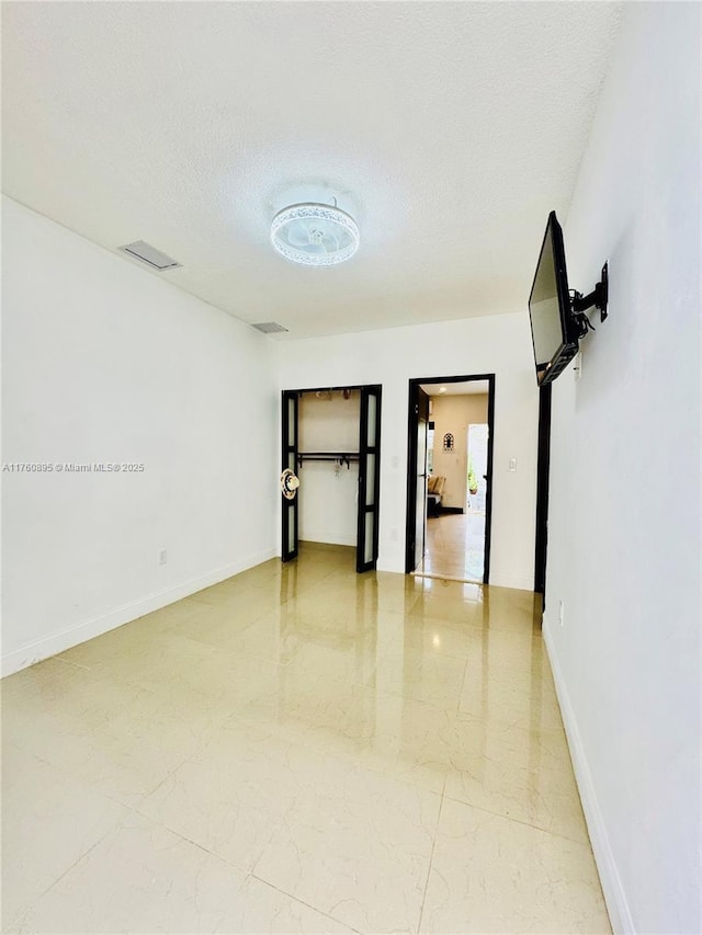 spare room with visible vents, baseboards, marble finish floor, and a textured ceiling