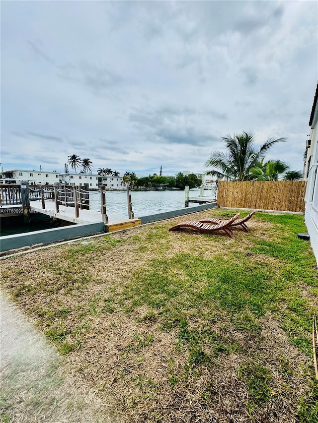 view of yard featuring fence, a water view, and a dock