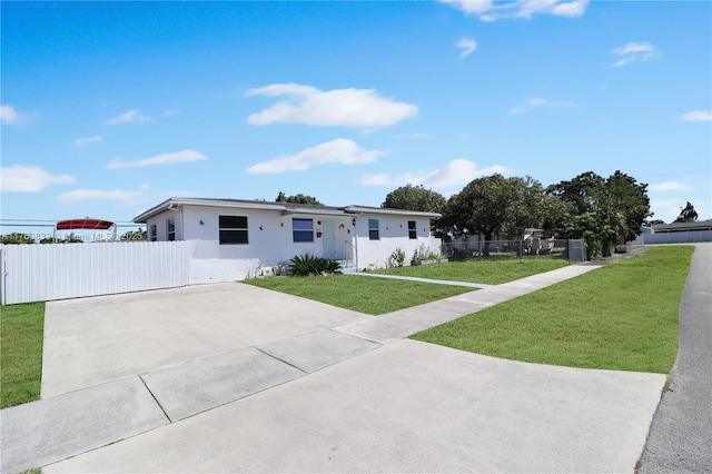 view of front of home with stucco siding, driveway, a front lawn, and fence