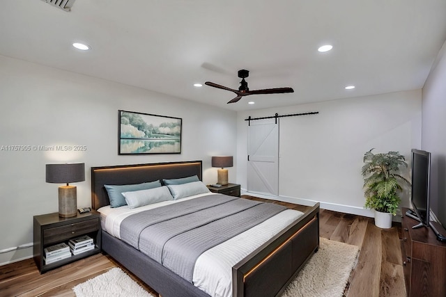 bedroom featuring recessed lighting, a barn door, baseboards, and wood finished floors