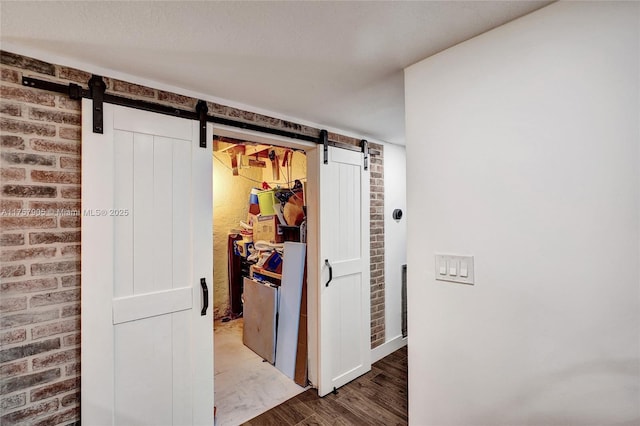 hallway with a barn door, wood finished floors, and brick wall