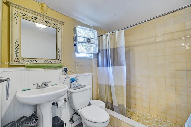 bathroom with a sink, a wainscoted wall, tiled shower, and toilet