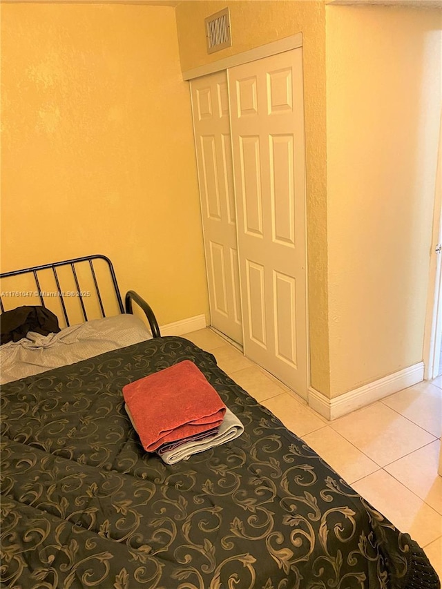 bedroom featuring light tile patterned flooring, visible vents, baseboards, and a closet