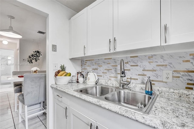 kitchen with tasteful backsplash, light stone counters, hanging light fixtures, white cabinets, and a sink