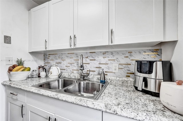 kitchen featuring white cabinets, light stone counters, backsplash, and a sink