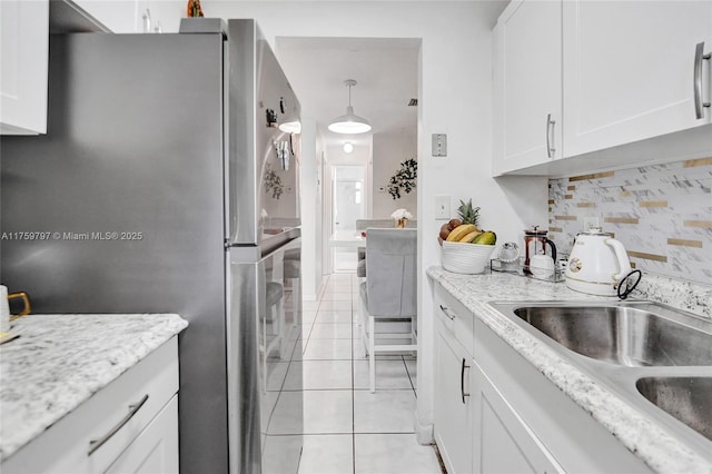 kitchen featuring a sink, freestanding refrigerator, white cabinets, light tile patterned floors, and decorative backsplash