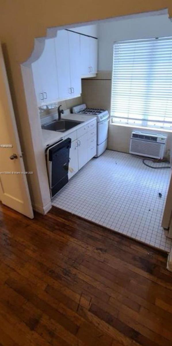 kitchen with dishwasher, hardwood / wood-style flooring, white gas stove, and a sink