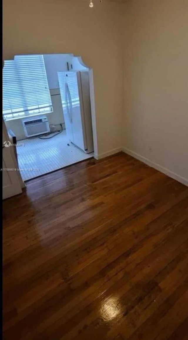 unfurnished room featuring baseboards, an AC wall unit, and wood finished floors