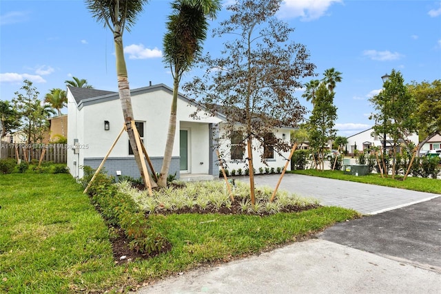 view of front facade with brick siding, fence, a front yard, stucco siding, and driveway