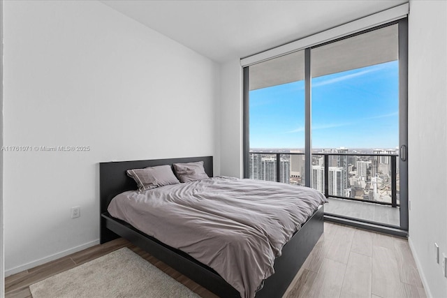 bedroom featuring access to exterior, wood finished floors, baseboards, and expansive windows