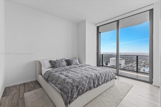 bedroom with access to exterior, a wall of windows, baseboards, and wood finished floors