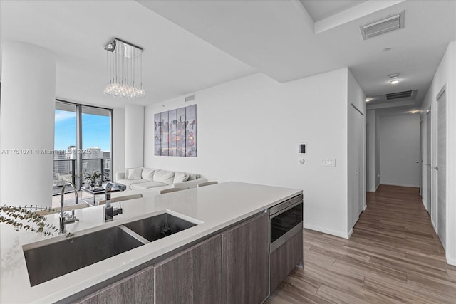 kitchen with visible vents, dark brown cabinetry, light countertops, light wood-style flooring, and a sink