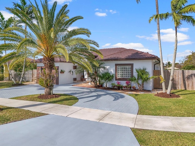 mediterranean / spanish home featuring a tiled roof, decorative driveway, fence, and stucco siding