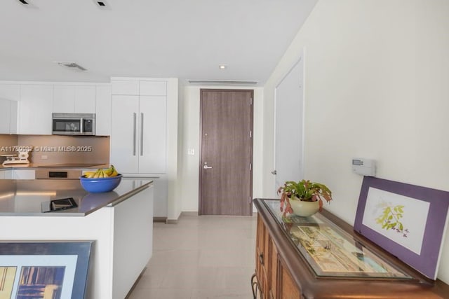 kitchen featuring dark countertops, visible vents, white cabinets, stainless steel microwave, and modern cabinets