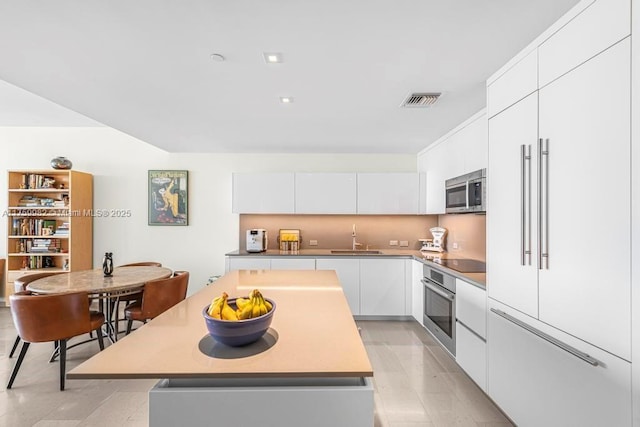 kitchen with modern cabinets, a sink, a center island, white cabinetry, and appliances with stainless steel finishes