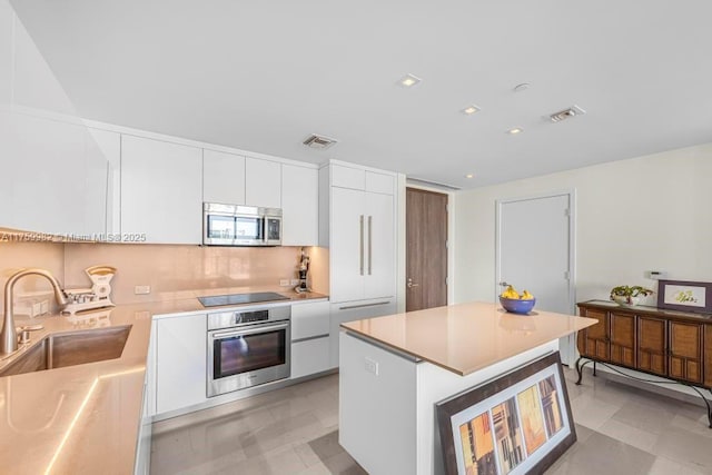 kitchen with a sink, light countertops, stainless steel appliances, white cabinetry, and modern cabinets