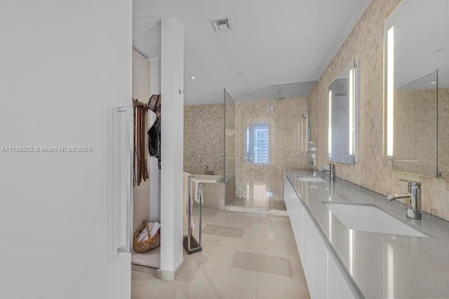 bathroom with visible vents, double vanity, a stall shower, a sink, and tile walls