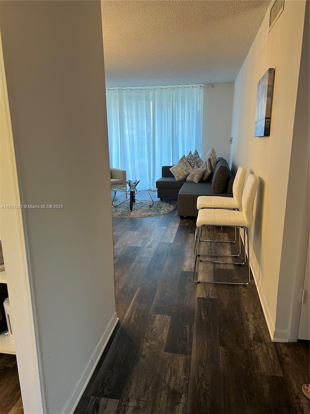 hallway featuring baseboards, wood finished floors, visible vents, and a textured ceiling