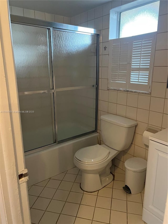 bathroom with vanity, enclosed tub / shower combo, tile patterned flooring, tile walls, and toilet