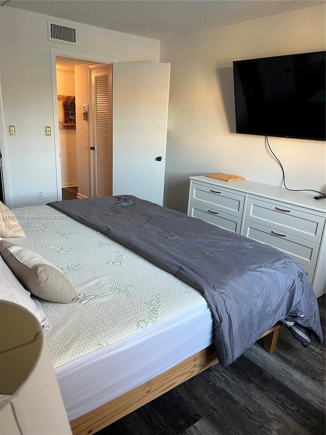 bedroom with visible vents, a textured ceiling, and wood finished floors