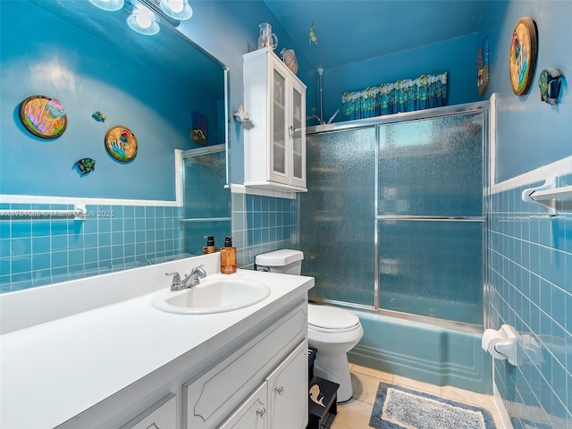 full bathroom featuring vanity, shower / bath combination with glass door, tile patterned flooring, tile walls, and toilet