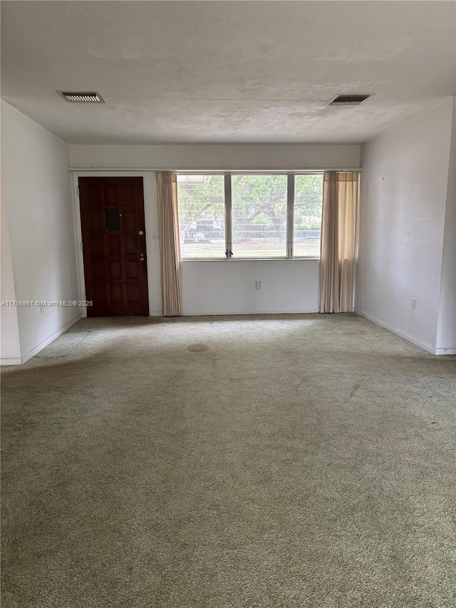 empty room featuring visible vents, baseboards, and carpet