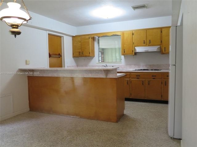 kitchen featuring under cabinet range hood, black stovetop, light countertops, brown cabinetry, and light speckled floor