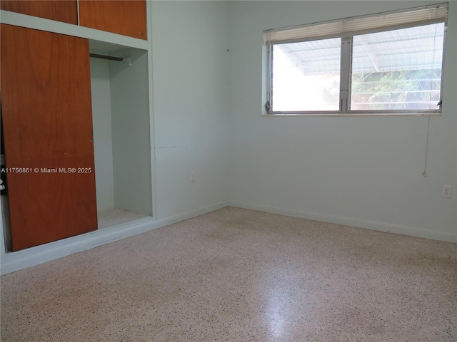 unfurnished bedroom featuring baseboards, speckled floor, and a closet