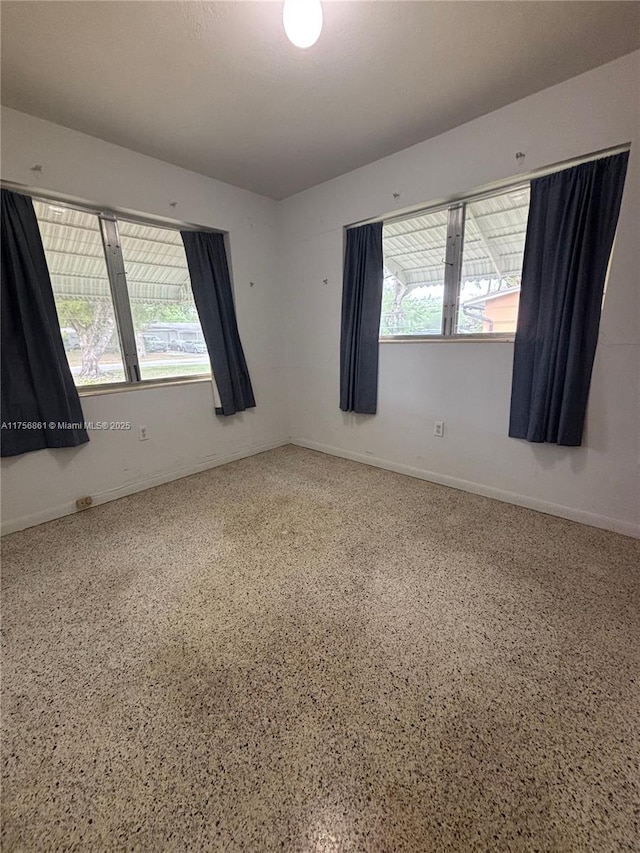 spare room featuring a healthy amount of sunlight, speckled floor, and baseboards