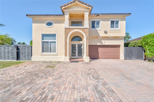 mediterranean / spanish-style house featuring fence, stucco siding, french doors, decorative driveway, and an attached garage