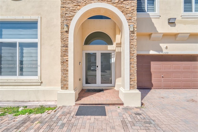 entrance to property featuring decorative driveway, french doors, a garage, and stucco siding