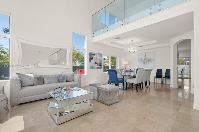 living area with baseboards, arched walkways, a towering ceiling, a raised ceiling, and a chandelier