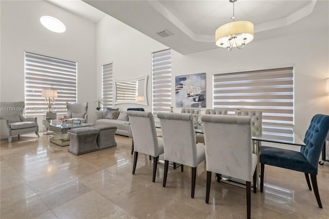 dining area with visible vents, an inviting chandelier, a high ceiling, and a tray ceiling