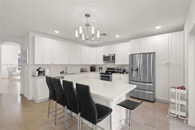 kitchen featuring a sink, arched walkways, appliances with stainless steel finishes, white cabinets, and light countertops