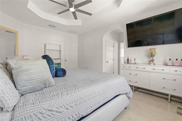 bedroom with visible vents, arched walkways, ceiling fan, a closet, and a raised ceiling