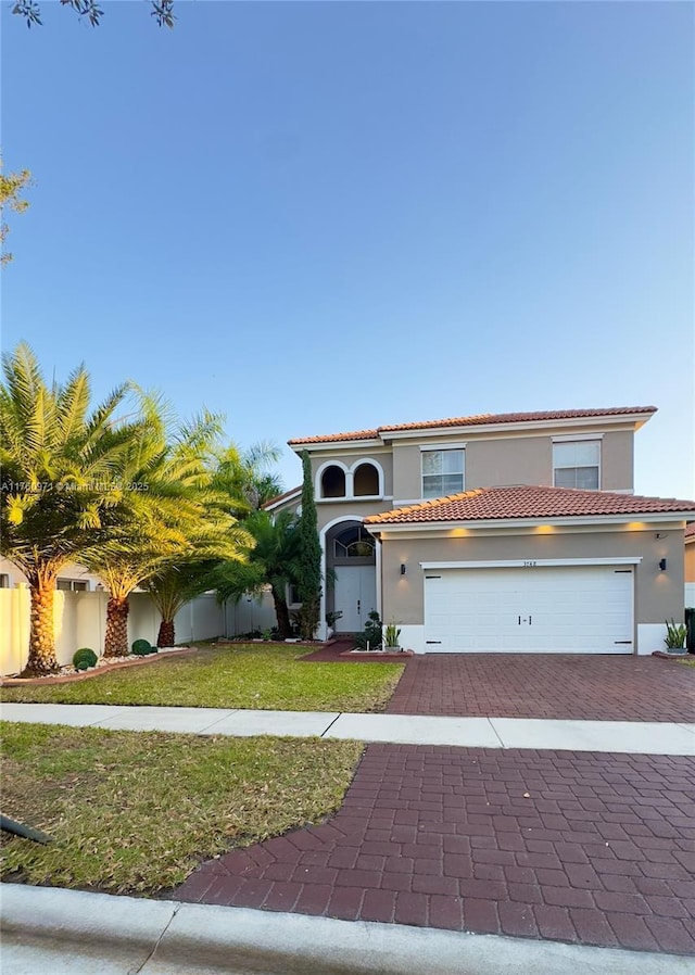 mediterranean / spanish-style house featuring an attached garage, stucco siding, a front lawn, a tile roof, and decorative driveway