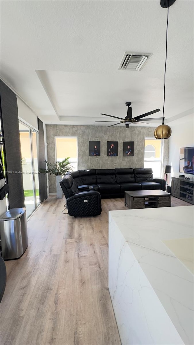 living area featuring a textured ceiling, ceiling fan, visible vents, and light wood-type flooring