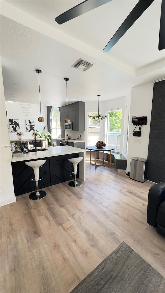 kitchen with visible vents, stainless steel microwave, a kitchen bar, light wood-type flooring, and light countertops