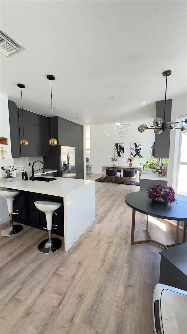 kitchen featuring light wood finished floors, visible vents, stainless steel fridge with ice dispenser, hanging light fixtures, and a sink